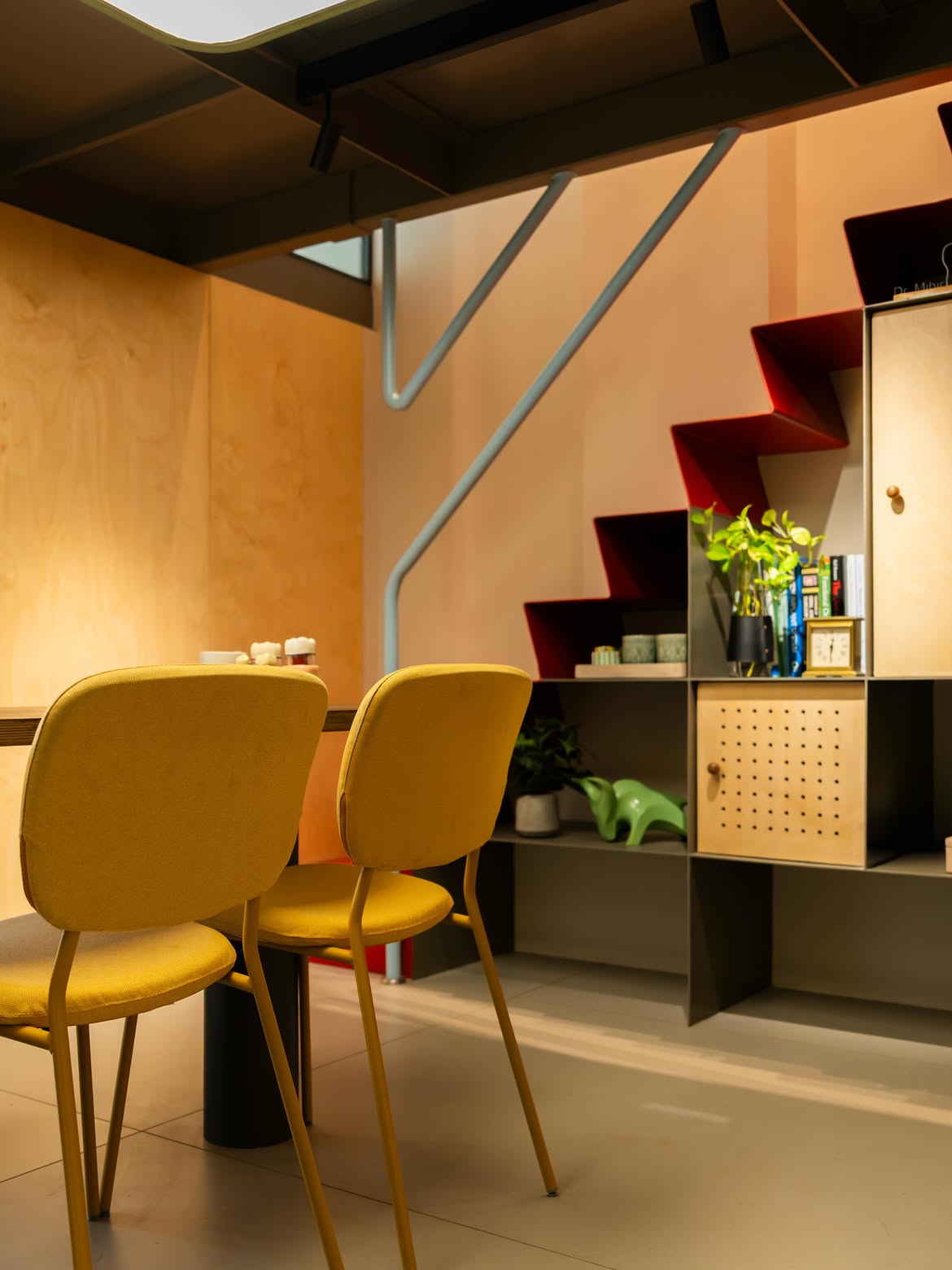 Cosy waiting nook with yellow chairs beneath the staircase display shelf
